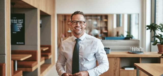 smiling-mature-businessman-standing-alone-in-an-of-2022-02-02-04-48-31-utc.jpg